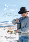 The cover of the book 'Winter Warmers' by Philippa Cameron, featuring a photograph of the author holding a mug, set against a backdrop of a snowy landscape.